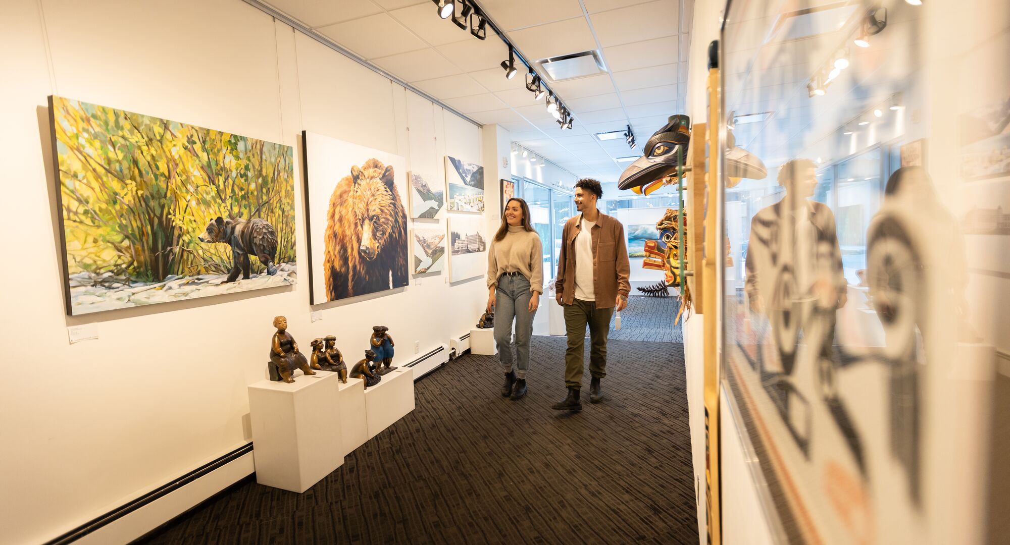 Two people walk through a gallery with art on both sides of bears in Banff National Park.
